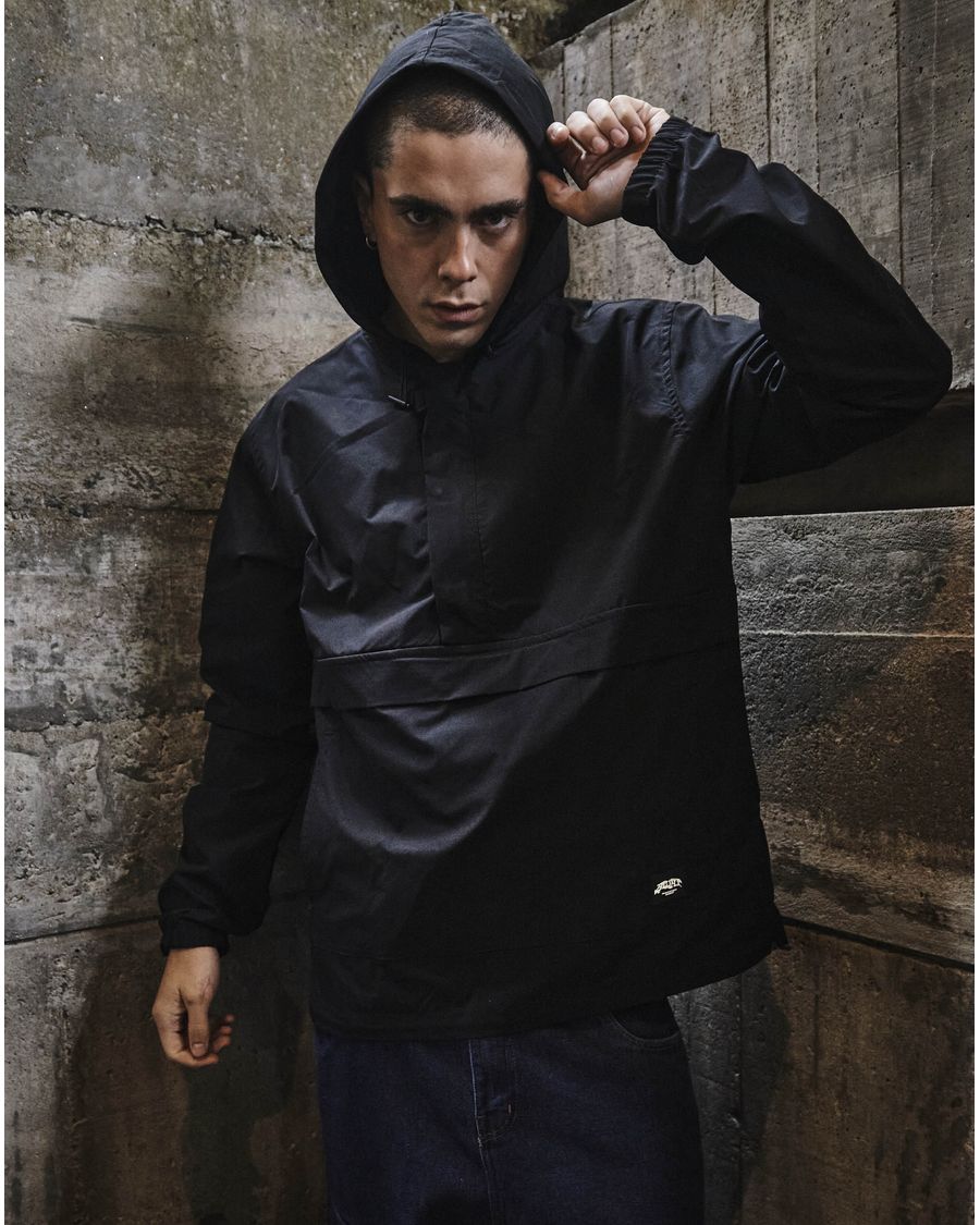 Anorak preto com capuz, em frente a um muro de concreto